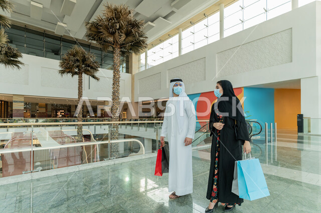 قضاء وقت ممتع في إحدى المولات التجارية، المشاركة في اختيارات التسوق وتبادل الآراء، زوجين عربيين خليجيين اماراتيين يضعان الكمامة للوقاية من فايروس كورونا ويحملان الأكياس الورقية الملونة، الإستفادة من العروض والتخفيضات الموسمية، الاستمتاع بالشراء والتبضع في المول