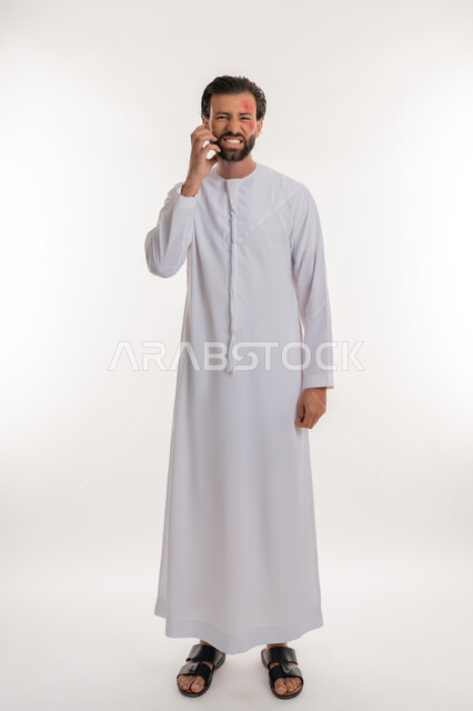 الإصابة بالحساسية الجلدية, بثور منتشرة على بشرة الوجه, بورتريه لرجل عربي خليجي اماراتي يرتدي الكندورة يقوم بالحك بإيماءات الإنزعاج والتعب, المشاكل الصحية والتهجيات، الشعور بالأوجاع والالام, صورة لكامل الجسم، خلفية بيضاء
