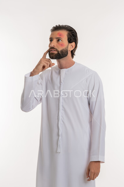 Skin rash and infectious diseases, need to visit a doctor and receive treatment, portrait of a young Arab Gulf Emirati man wearing a kandura pointing to the location of the disease, health problems and skin irritations, pimples spread on the skin of the face, skin infection and hypersensitivity, white background