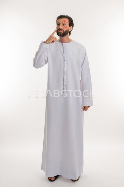 الحاجة لزيارة الطبيب وتلقي العلاج, الطفح الجلدي والأمراض المعدية, بورتريه لشاب عربي خليجي اماراتي يرتدي الكندورة يشير لمكان المرض, المشاكل الصحية وتهيجات الجلد, بثور منتشرة على بشرة الوجه, الإصابة الجلدية وفرط التحسس, صورة لكامل الجسم، خلفية بيضاء
