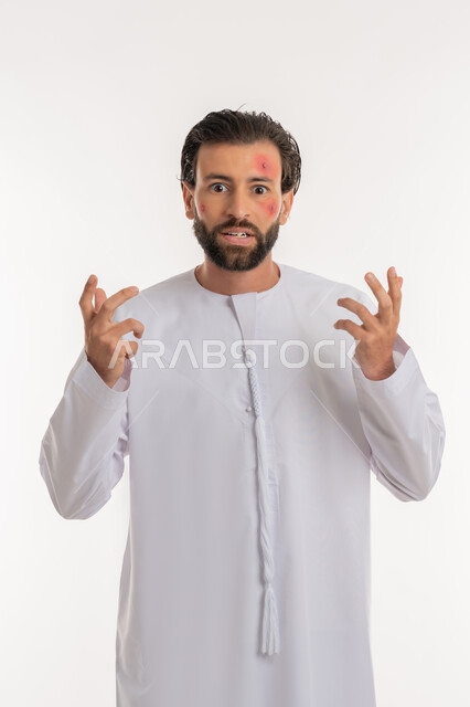 Expressions of stress and discomfort, skin rash and infectious diseases, portrait of a young Arab Gulf Emirati man wearing a kandura raising his hands up, health problems and skin irritations, pimples spread on the skin of the face, skin infection and hypersensitivity, white background