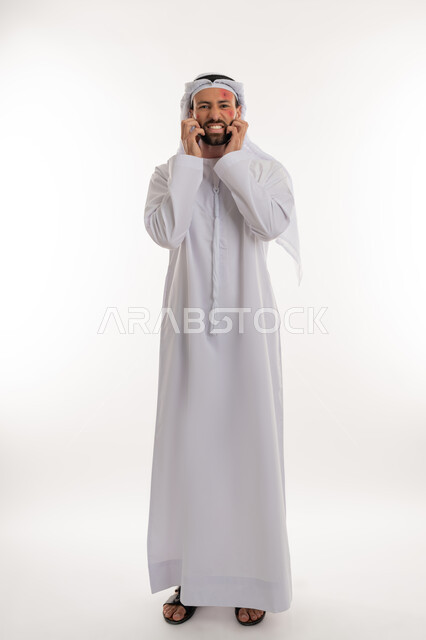 تهيجات الجلد والمشاكل الصحية, فرط التحسس والإصابة الجلدية, الأمراض المعدية والطفح الجلدي, الحاجة لزيارة الطبيب وتلقي العلاج, بورتريه لشاب عربي خليجي اماراتي يرتدي الكندورة والغترة يقوم بالحك بإيماءات الإنزعاج, بثور منتشرة على بشرة الوجه, صورة لكامل الجسم، خلفية بيضاء