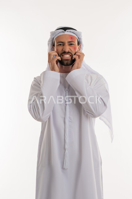 الأمراض المعدية والطفح الجلدي, تهيجات الجلد والمشاكل الصحية, فرط التحسس والإصابة الجلدية, الحاجة لزيارة الطبيب وتلقي العلاج, بورتريه لشاب عربي خليجي اماراتي يرتدي الكندورة والغترة يقوم بالحك بإيماءات الإنزعاج, بثور منتشرة على بشرة الوجه, خلفية بيضاء