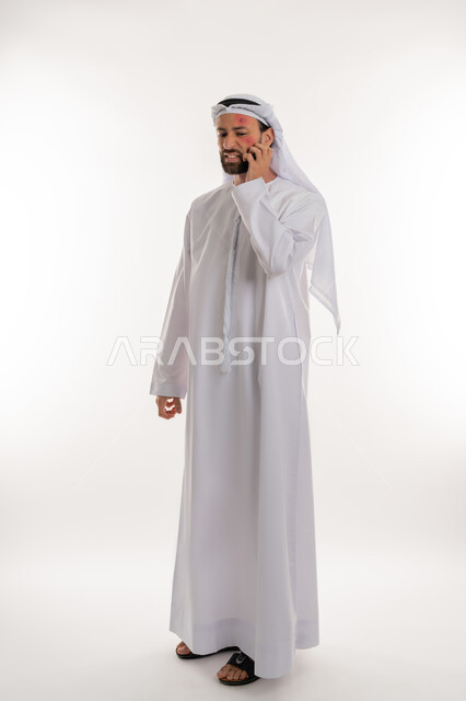 الحاجة لزيارة الطبيب وتلقي العلاج, الأمراض المعدية والطفح الجلدي, فرط التحسس والإصابة الجلدية, بورتريه من الجانب لشاب عربي خليجي اماراتي يرتدي الكندورة والغترة يقوم بالحك بإيماءات الإنزعاج, بثور منتشرة على بشرة الوجه, صورة لكامل الجسم، خلفية بيضاء