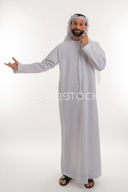 عدم المعرفة بامر ما, الإشارة إلى مكان المرض, بثور منتشرة على بشرة الوجه, بورتريه لرجل عربي خليجي اماراتي يرتدي الكندورة والغترة يرفع يده بايماءات الجهل, الإصابة بالحساسية الجلدية, المشاكل الصحية والتهجيات، صورة لكامل الجسم، خلفية بيضاء