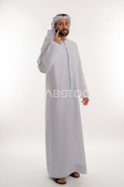 الشعور بالأوجاع والالام, الإشارة إلى مكان المرض, بثور منتشرة على بشرة الوجه, بورتريه من الجانب لرجل عربي خليجي اماراتي يرتدي الكندورة والغترة ينظر لمكان ما بإيماءات الإنزعاج, الإصابة بالحساسية الجلدية, المشاكل الصحية والتهجيات، صورة لكامل الجسم، خلفية بيضاء