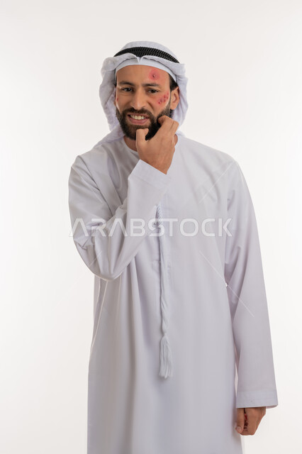 تهيجات الجلد والمشاكل الصحية, فرط التحسس والإصابة الجلدية, الأمراض المعدية والطفح الجلدي, الحاجة لزيارة الطبيب وتلقي العلاج, بورتريه لشاب عربي خليجي اماراتي يرتدي الكندورة والغترة يقوم بالحك بإيماءات الإنزعاج, بثور منتشرة على بشرة الوجه, خلفية بيضاء
