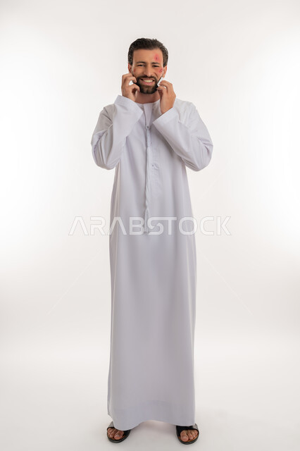 الإصابة بالحساسية الجلدية, بثور منتشرة على بشرة الوجه, بورتريه لرجل عربي خليجي اماراتي يرتدي الكندورة يقوم بالحك بإيماءات الإنزعاج والتعب, المشاكل الصحية والتهجيات، الشعور بالأوجاع والالام, صورة لكامل الجسم، خلفية بيضاء