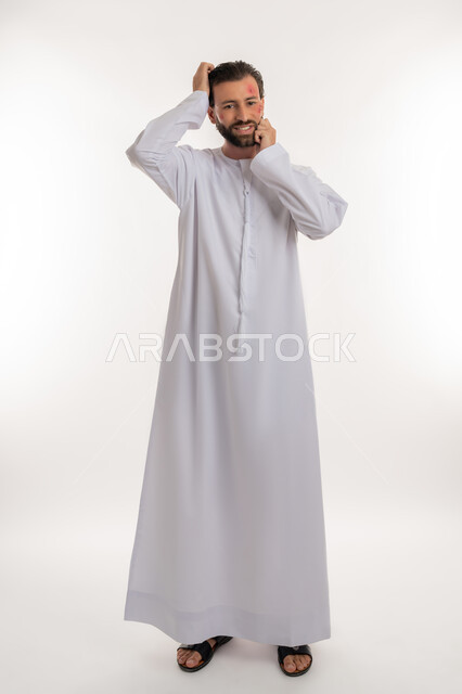 الأمراض المعدية والطفح الجلدي, الحاجة لزيارة الطبيب وتلقي العلاج, بورتريه لشاب عربي خليجي اماراتي يرتدي الكندورة يقوم بالحك بإيماءات الإنزعاج, تهيجات الجلد والمشاكل الصحية, بثور منتشرة على بشرة الوجه, فرط التحسس والإصابة الجلدية, صورة لكامل الجسم، خلفية بيضاء