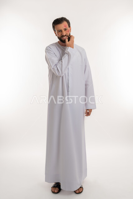 الإصابة بالحساسية الجلدية, بثور منتشرة على بشرة الوجه, بورتريه لرجل عربي خليجي اماراتي يرتدي الكندورة يقوم بالحك بإيماءات الإنزعاج والتعب, المشاكل الصحية والتهجيات، الشعور بالأوجاع والالام, صورة لكامل الجسم، خلفية بيضاء