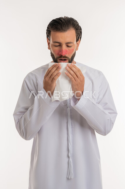 الشعور بالمرض و الزكام والحاجة الى العلاج والدواء, التهاب الأنف التحسسي, استخدام المناديل الورقيه للعطس, بورتريه لشاب عربي خليجي اماراتي يرتدي الكندورة يرفع يديه على وجهه بإيماءات العطاس, خلفية بيضاء