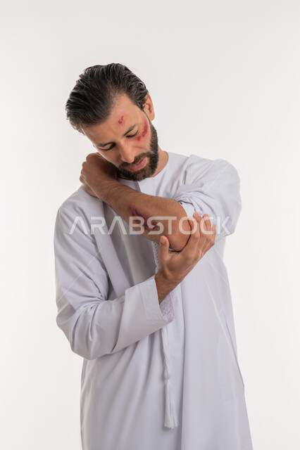 Physical injuries and bruises, exposure to violence and harm, feeling severe pain, need for home medical care, portrait of an injured Arab Gulf Emirati man wearing a kandura looking at the wounds with expressions of fatigue and exhaustion, white background