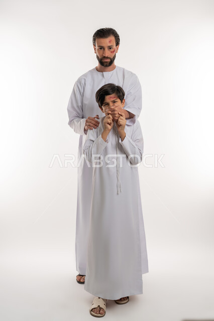 الغضب والسلوك العدواني, اصابات و جروح جسدية، قضايا اجتماعيه أسريه، المشاكل والخلافات الاسرية، بورتريه لولد عربي خليجي اماراتي يرتدي الكندورة يتعرض للعنف من قبل والده، ايماءات الآلم والحزن، صورة لكامل الجسم، خلفية بيضاء