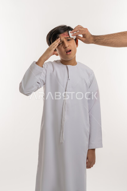 الاصابة بالجروح والكدمات، تلقي الرعاية الطبية، الشعور بالتعب والارهاق، التعرض للعنف والاذى، بورتريه لفتى عربي خليجي اماراتي يرتدي الكندورة يضع يده على رأسه  بايماءات الالم الشديد، خلفية بيضاء