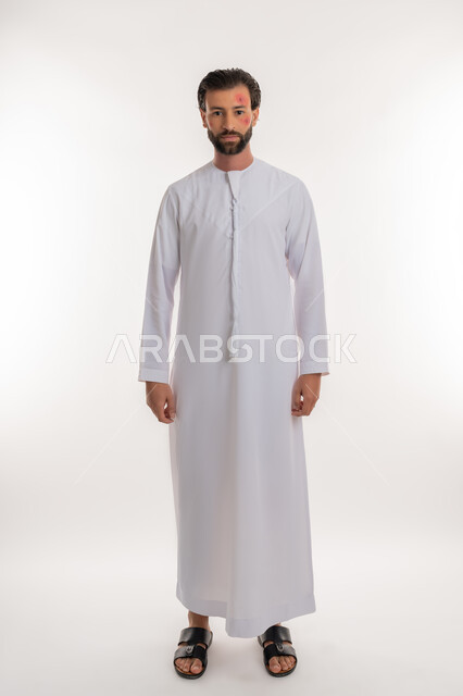 النظر الى الكاميرا بتعابير التعب والارهاق، المشاكل الصحية والتهجيات، الإصابة بالحساسية الجلدية, بثور منتشرة على بشرة الوجه, بورتريه لرجل عربي خليجي اماراتي يرتدي الكندورة يقف باستقامة, الشعور بالأوجاع والالام, صورة لكامل الجسم، خلفية بيضاء