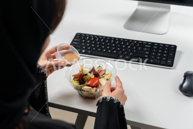 Diet for a slim body and ideal weight, delicious cold appetizers, close-up photo of a veiled Emirati Gulf Arab woman wearing a black abaya sitting on a comfortable chair eating, a complete healthy meal consisting of fresh vegetable salad