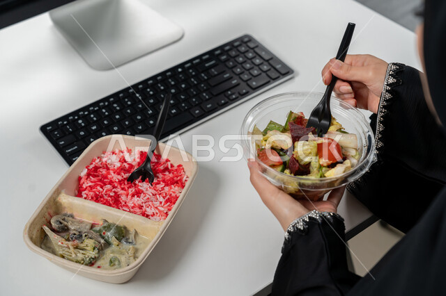 مقبلات باردة و وجبات ساخنة, وجبة صحية متكاملة مكونة من سلطة الخضروات الطازجة وطبق من الأرز الصحي , حمية غذائية لجسم رشيق ووزن مثالي , صورة مقربة لامراة عربية خليجية اماراتية محجبة ترتدي عباءة سوداء تجلس على كرسي مريح تقوم بتناول الطعام