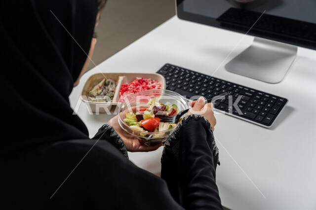 مقبلات باردة و وجبات ساخنة, وجبة صحية متكاملة مكونة من سلطة الخضروات الطازجة وطبق من الأرز الصحي , حمية غذائية لجسم رشيق ووزن مثالي , صورة مقربة لامراة عربية خليجية اماراتية محجبة ترتدي عباءة سوداء تجلس على كرسي مريح تقوم بتناول الطعام