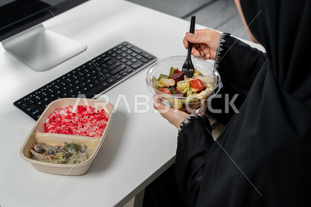 مقبلات باردة و وجبات ساخنة, وجبة صحية متكاملة مكونة من سلطة الخضروات الطازجة وطبق من الأرز الصحي , حمية غذائية لجسم رشيق ووزن مثالي , صورة مقربة لامراة عربية خليجية اماراتية محجبة ترتدي عباءة سوداء تجلس على كرسي مريح تقوم بتناول الطعام
