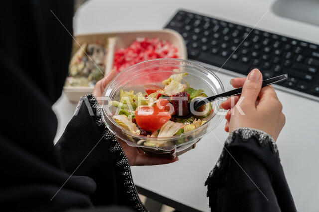 مقبلات باردة و وجبات ساخنة, وجبة صحية متكاملة مكونة من سلطة الخضروات الطازجة وطبق من الأرز الصحي , حمية غذائية لجسم رشيق ووزن مثالي , صورة مقربة لامراة عربية خليجية اماراتية محجبة ترتدي عباءة سوداء تجلس على كرسي مريح تقوم بتناول الطعام