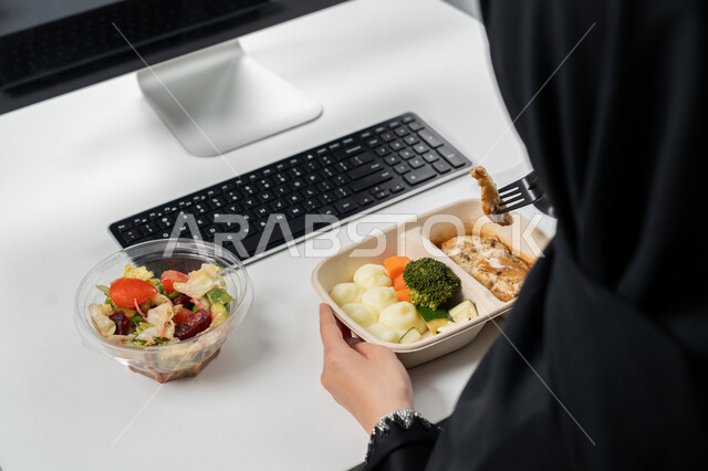 وجبات ساخنة و مقبلات باردة, وجبة صحية متكاملة مكونة من سلطة الخضروات الطازجة وطبق من الدجاج مع الخضار , حمية غذائية لجسم رشيق ووزن مثالي ,  صورة مقربة لامراة عربية خليجية اماراتية محجبة ترتدي عباءة سوداء تجلس على كرسي مريح تقوم بتناول الطعام