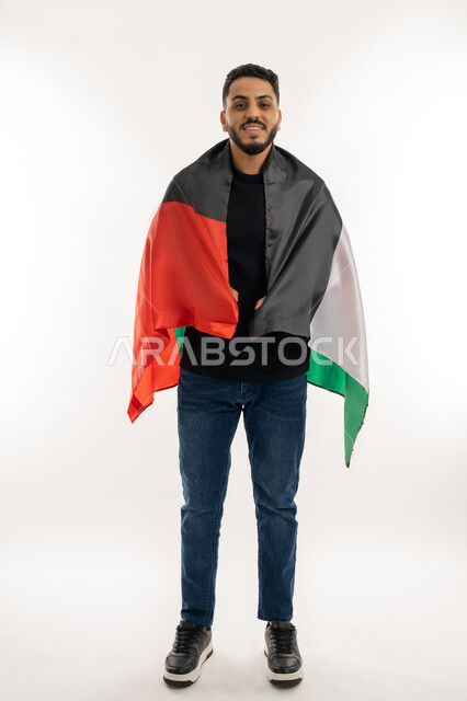 Commemorating the Independence of the Emirates, looking at the camera with gestures of pride and confidence, the identity of the 51st UAE National Day, a portrait of a young Arab Gulf Emirati man wearing casual clothes carrying the UAE flag on his back, love and belonging to the homeland, full body, white background