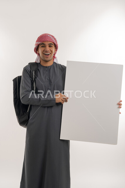 النظر إلى الكاميرا بإيماءات السعادة والسرور, استخدام لوحات توضيحية ووسائل تعليمية, موك اب مستطيل فارغ، بورتريه لطالب جامعي عربي خليجي إماراتي يرتدي الكندورة والعمامة يحمل بيده لوح أبيض كبير, خلفية رمادية