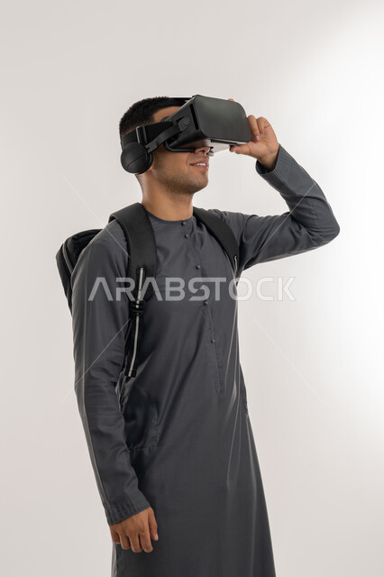 منصات تعليميه تعتمد على الواقع الافتراضي, التعليم بواسطة خاصية الهولوجرام ثلاثية الابعاد, محاكاة العالم الخيالي, بورتريه لطالب جامعي عربي خليجي إماراتي يرتدي الكندورة يضع نظارة الفي ار ثلاثية الابعاد, خلفية رمادية
