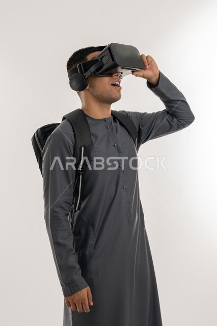 منصات تعليميه تعتمد على الواقع الافتراضي, التعليم بواسطة خاصية الهولوجرام ثلاثية الابعاد, محاكاة العالم الخيالي, بورتريه لطالب جامعي عربي خليجي إماراتي يرتدي الكندورة يضع نظارة الفي ار ثلاثية الابعاد, خلفية رمادية