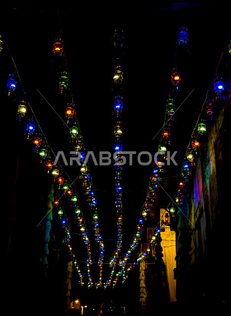 صورة لمجموعة من الفوانيس الملونة المضيئة المعلقة بشوارع جدة القديمة ليلا ، مدينة جدة القديمة ذات التصميم المعماري العربي والاسلامي القديم المزينة بأجواء رمضانية أماكن سياحية ، المملكة العربية السعودية