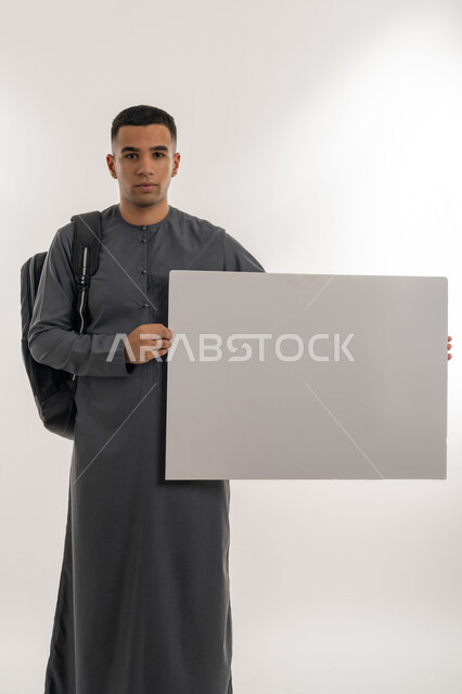 Higher education in UAE academic universities and colleges, using illustrations and educational tools, empty rectangular mockup, portrait of an Arab Gulf Emirati university student wearing a kandura carrying a bag on his back and holding a large white board, gray background