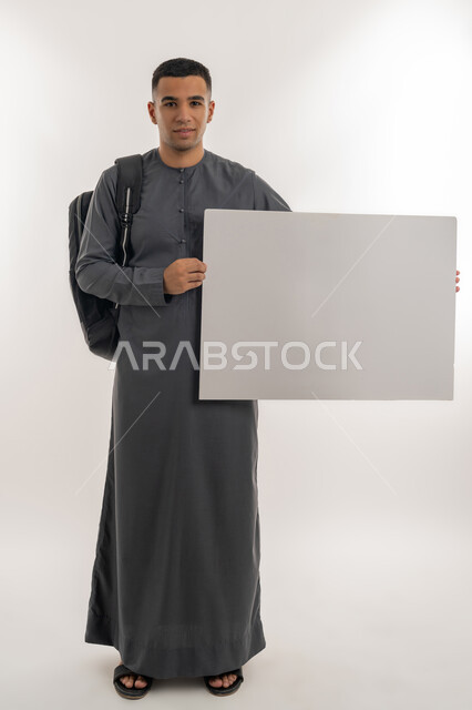Using illustrations and educational tools, Empty rectangular mockup, Higher education in UAE academic universities and colleges, Portrait of an Emirati Gulf Arab university student wearing a kandura carrying a bag on his back and holding a large white board, full body, gray background