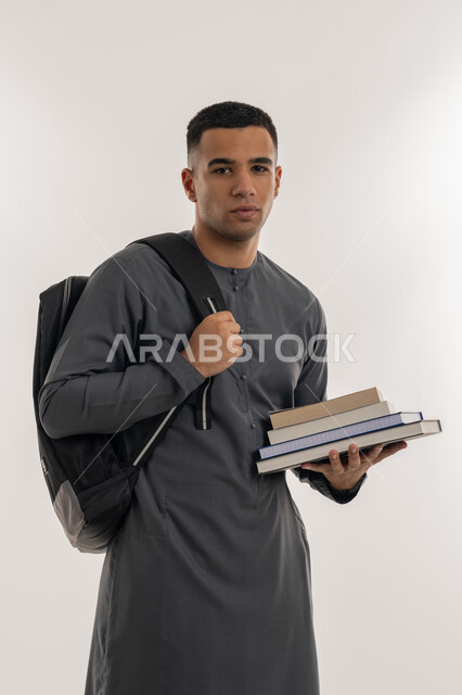 التعليم العالي في الجامعات في الإمارات العربية المتحدة, المناهج والمواد التعليمية, الاستعداد للعام الجامعي الجديد, بورتريه لطالب جامعي عربي خليجي إماراتي يرتدي الكندورة ينظر إلى الكاميرا ويحمل حقيبة على ظهره وبيده الكتب, خلفية رمادية