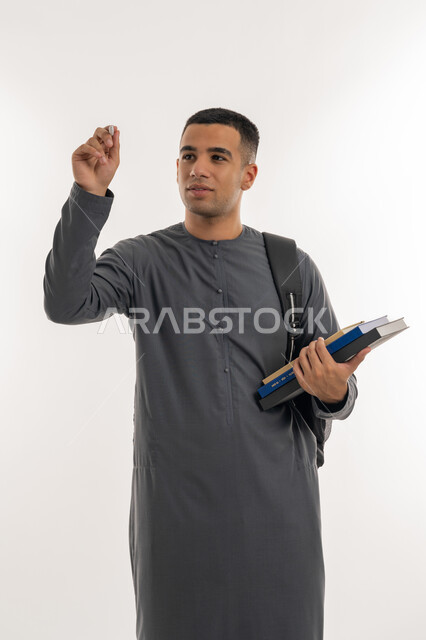 محاولة كتابة شيء ما, التعليم العالي في الجامعات والكليات الأكاديمية الإماراتية, بورتريه لطالب جامعي عربي خليجي إماراتي يرتدي الكندورة يحمل حقيبة على ظهره وبيديه الكتب و القلم, خلفية رمادية