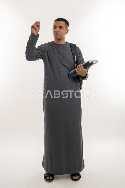 محاولة كتابة شيء ما, التعليم العالي في الجامعات والكليات الأكاديمية الإماراتية, بورتريه لطالب جامعي عربي خليجي إماراتي يرتدي الكندورة يحمل حقيبة على ظهره وبيديه كتب وقلم, الجسم بالطول الكامل, خلفية رمادية