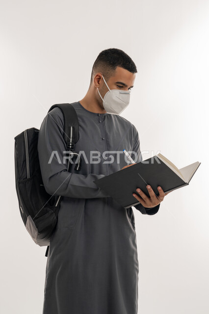 القيام بالإجراءات الوقائية لتجنب الإصابة بفايروس كورونا, نشر الوعي الصحي، التعليم الجامعي في الإمارات، بورتريه لطالب جامعي عربي خليجي إماراتي يرتدي الكندورة والكمامة يحمل حقيبة على ظهره ويقوم بتدوين الملاحظات, خلفية رمادية