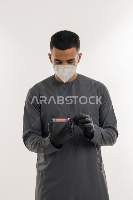نشر الوعي الصحي للحد من انتشار الأمراض, اتباع الإجراءات الاحترازية للوقاية من فايروس كورونا، التطعيم الآمن لكوفيد19، بورتريه لطالب جامعي عربي خليجي إماراتي يرتدي الكندورة والكمامة يحمل بيده إبرة لقاح, خلفية رمادية