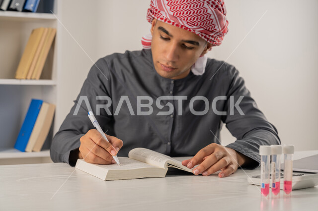 التعليم الجامعي في الإمارات العربية المتحدة, مفهوم الاجتهاد والتفوق, المناهج والمواد التعليمية, بورتريه مقرب لطالب جامعي عربي خليجي إماراتي يرتدي الكندورة والعمامة يجلس على الطاولة في مكتبة الجامعة ويقوم بالكتابة ومراجعة الدروس اليومية, خلفية رمادية