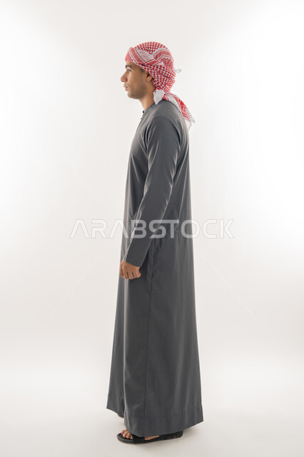مفهوم الأناقة والرجولة, الاهتمام بالمظهر الخارجي, بورتريه من الجانب لشاب عربي خليجي إماراتي يرتدي الكندورة والعمامة يقف باستقامة واعتدال, الجسم بالطول الكامل, خلفية بيضاء