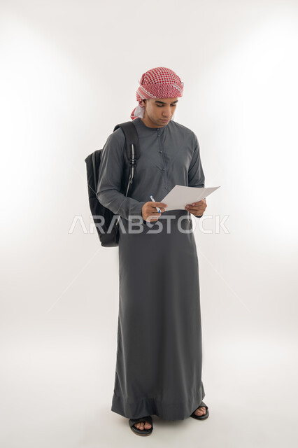 الاستعداد للعام الجامعي الجديد, الجامعات والكليات الأكاديمية الإماراتية, بورتريه لطالب جامعي عربي خليجي إماراتي يرتدي الكندرورة والعمامة يحمل حقيبة على ظهره يمسك بيده ورقة وقلم يقوم بمتابعة الدروس اليومية, الجسم بالطول الكامل, خلفية بيضاء