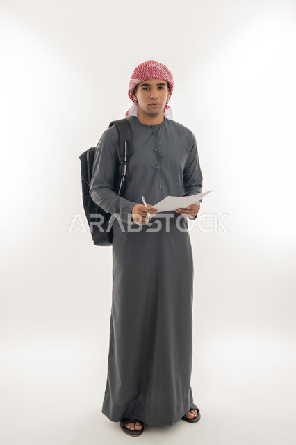 الاستعداد للعام الجامعي الجديد, الجامعات والكليات الأكاديمية الإماراتية, بورتريه لطالب جامعي عربي خليجي إماراتي يرتدي الكندرورة والعمامة يحمل حقيبة على ظهره يمسك بيده ورقة وقلم يقوم بمتابعة الدروس اليومية, الجسم بالطول الكامل, خلفية بيضاء