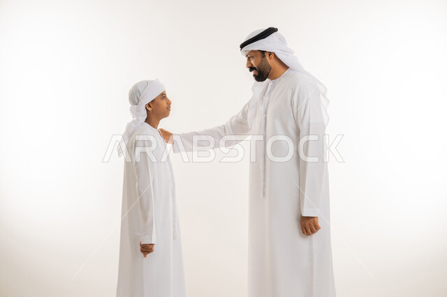 ايماءات الحب والعطف على الأبناء، تعابير السعادة والسرور، تحمل المسؤولية والاعتناء بالأولاد، مفهوم الرابطة الأبوية والترابط الأسري، بورتريه مقرب من الجانب لرجل عربي خليجي اماراتي يرتدي الكندورة والغترة يضع يده على كتف ابنه، خلفية بيضاء