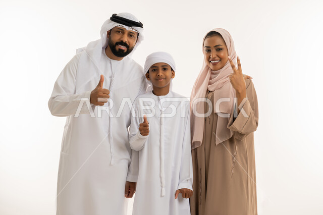 تعابير الإعجاب والقبول، النجاح وتحقيق الأهداف، الترابط الأسري والحفاظ على الاستقرار العائلي، رعاية الآباء بأبنائهم والاهتمام بهم، بورتريه مقرب لعائلة عربية اماراتية يرفعون اصبع الابهام للأعلى بهدف الرضا والموافقة، النظر للكاميرا بإيماءات السعادة، خلفية بيضاء