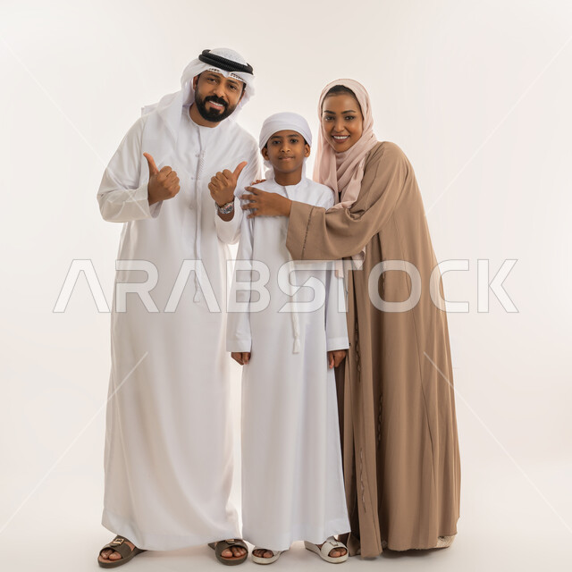 رعاية الآباء بأبنائهم والاهتمام بهم، تعابير الإعجاب والقبول، الترابط الأسري والحفاظ على الاستقرار العائلي، بورتريه لعائلة عربية اماراتية رجل يرفع اصبع الابهام للأعلى بهدف الرضا والموافقة، النظر للكاميرا بإيماءات السعادة، صورة الجسم بالطول الكامل، خلفية بيضاء