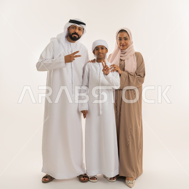 مفهوم الفوز والانتصار، تعابير السعادة بالوصول الى الغايات، النجاح وتحقيق الأهداف، الألفة والمحبة بين الأفراد، بورتريه لعائلة عربية خليجية اماراتية يرفعون ايديهم بإشارة النصر والقوة، النظر للكاميرا بإيماءات الثقة بالنفس، صورة الجسم بالطول الكامل، خلفية بيضاء