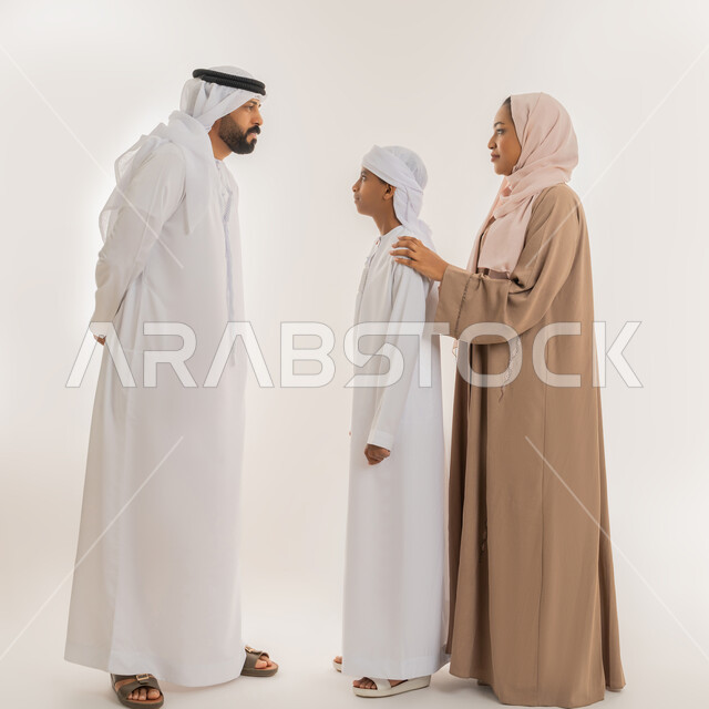 ايماءات التوبيخ والتنبيه، الوقوف بجدية والأمر بالتوقف عن فعل شيء ما، بورتريه لرجل عربي خليجي اماراتي يرتدي الكندورة والغترة قف برفقة زوجته وابنه وينظر الى ولده بهدف التهديد والتوعد والنهي عن أمر معين، صورة الجسم بالطول الكامل، خلفية بيضاء