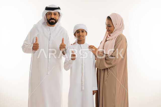تعابير الإعجاب والقبول، الترابط الأسري والحفاظ على الاستقرار العائلي، رعاية الآباء بأبنائهم والاهتمام بهم، بورتريه مقرب لعائلة عربية اماراتية يرفعوا اصبع الابهام للأعلى بهدف الرضا والموافقة، النظر للكاميرا بإيماءات السعادة، خلفية بيضاء