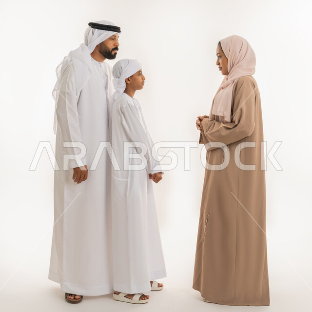 الوقوف بجدية والأمر بالتوقف عن فعل شيء ما، ايماءات التوبيخ والتنبيه، بورتريه لإمرأة عربية خليجية اماراتية ترتدي الحجاب والعباءة تقف برفقة زوجها وابنها وتنظر الى ولدها بهدف التهديد والتوعد والنهي عن أمر معين، صورة الجسم بالطول الكامل، خلفية بيضاء