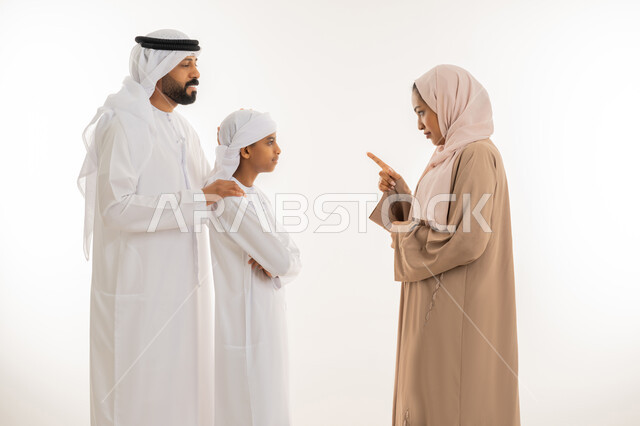 الوقوف بجدية والأمر بالتوقف عن فعل شيء ما، ايماءات التوبيخ والتنبيه، بورتريه مقرب لإمرأة عربية خليجية اماراتية ترتدي الحجاب والعباءة تقف برفقة زوجها وابنها وترفع اصبع السبابة الى الأعلى بهدف التهديد والتوعد والنهي عن أمر معين، خلفية بيضاء