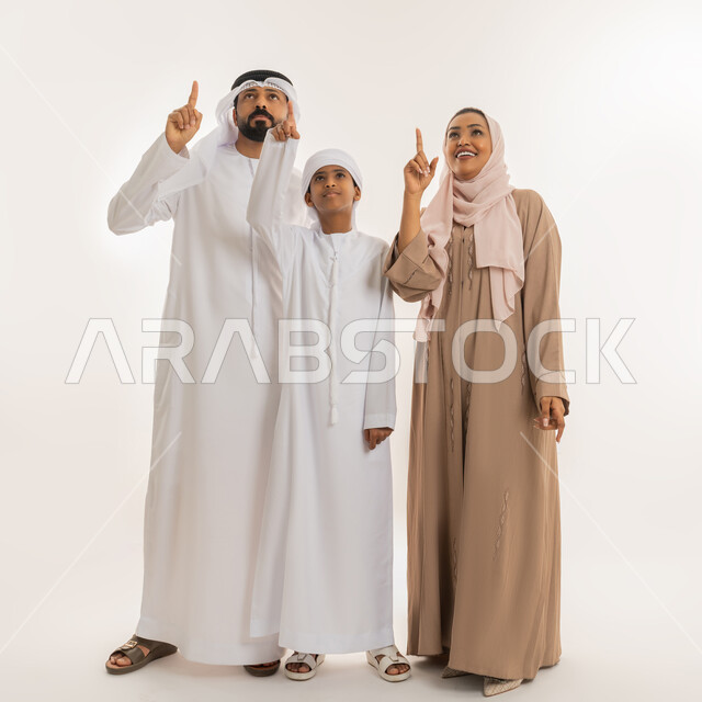 رعاية لآباء بالأبناء والاهتمام بهم، النظر الى مكان معين، التوجه والإشارة الى شيء ما، مفهوم لغة الجسد، بورتريه لعائلة عربية خليجية اماراتية يشيروا بإصبع السبابة الى الأعلى دلالة على موقع محدد، صورة الجسم بالطول الكامل، خلفية بيضاء